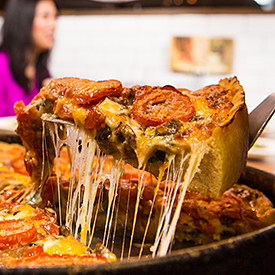 Slice of deep dish pizza being lifted from the pan