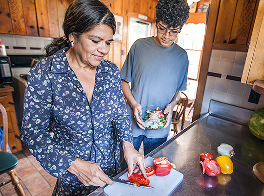 Latina woman cutting up vegetables with grandson
